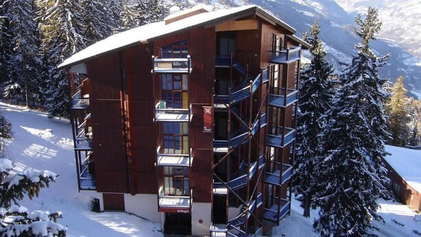 Ein Holzbalkonbau mit mehreren Balkonen und einer Skipiste im Hintergrund.
