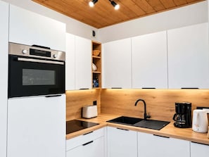 A modern kitchen with white cabinetry, a black countertop, a built-in oven, a sink, and a coffee maker. - 150m from ski slopes, 3rd floor, tv, 95m², Peisey-Vallandry (Landry)