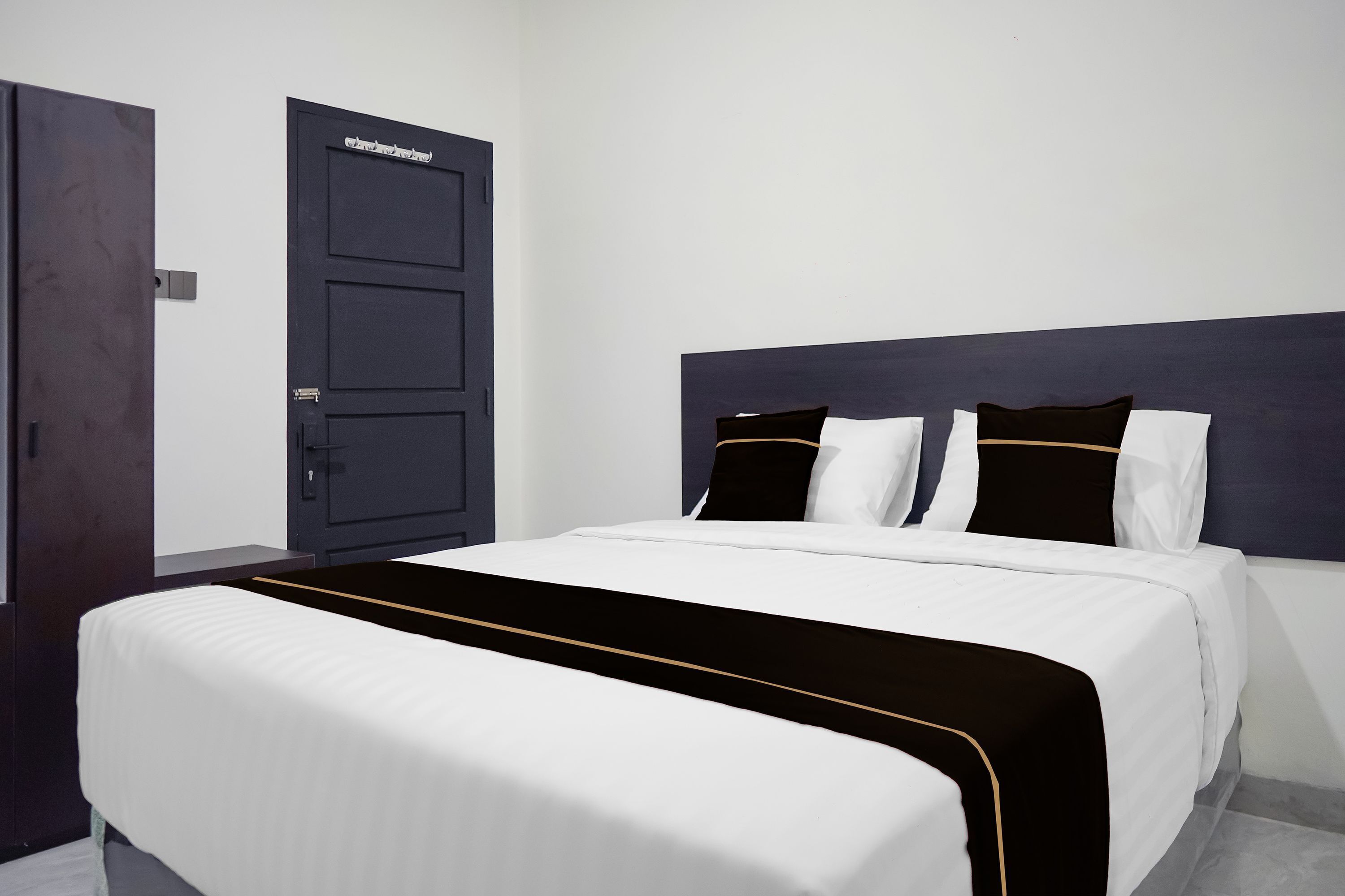 A hotel room with a large bed, a dark headboard, and a door with a sign.