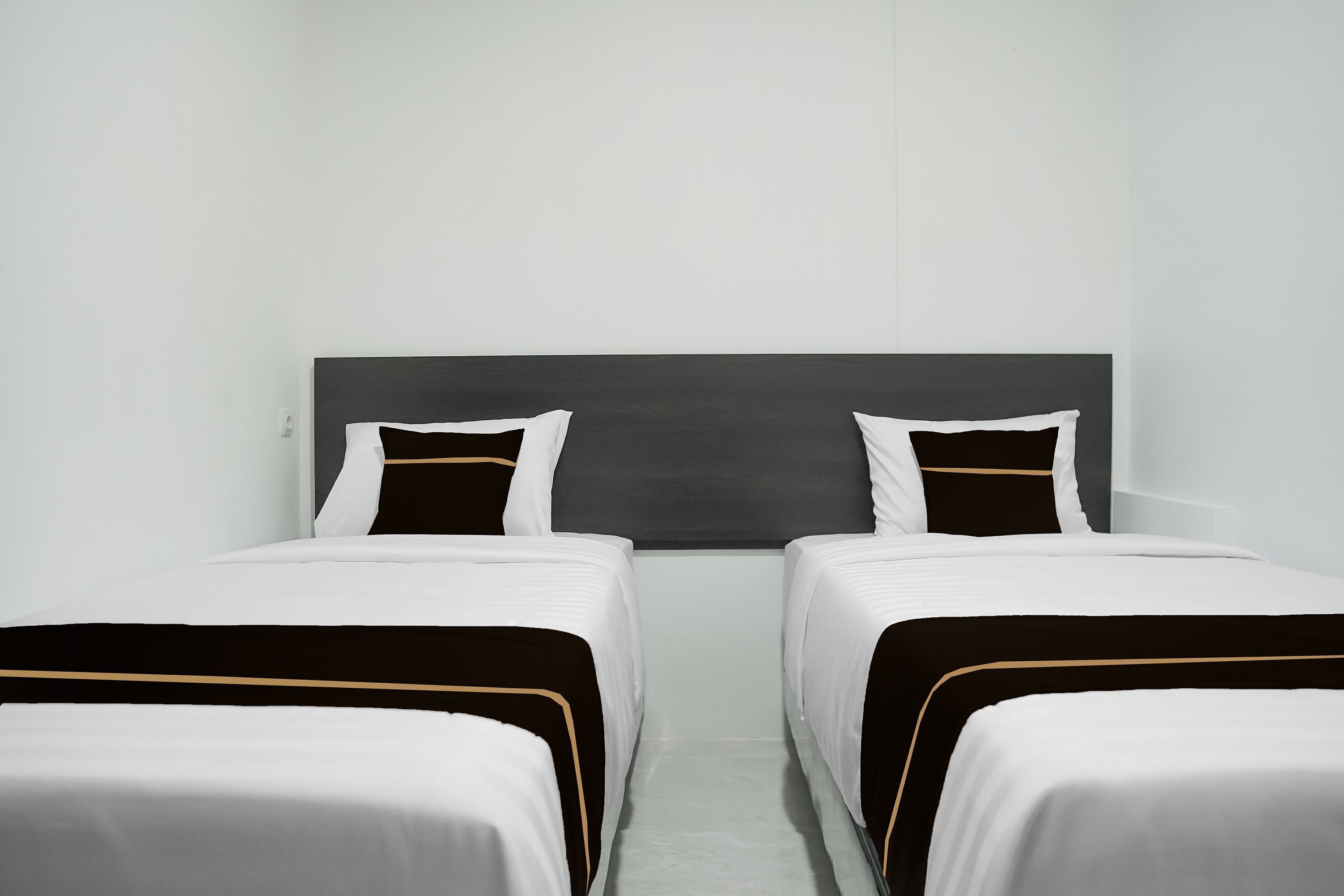 A hotel room with two single beds, a dark headboard, and a plain white wall.