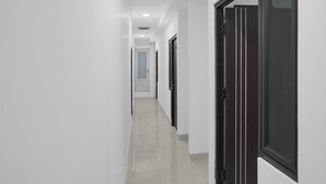 Un passadís amb parets blanques i un terra de rajola, que condueix a una porta amb finestreta.