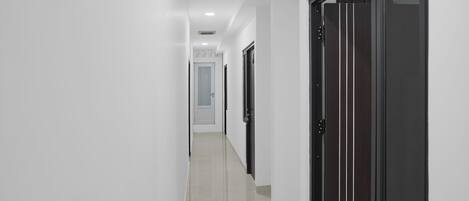 A hallway with white walls and a tiled floor, leading to a door with a window.
