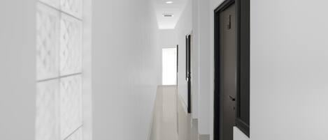 A corridor with white walls and a tiled floor, leading to a door at the end.