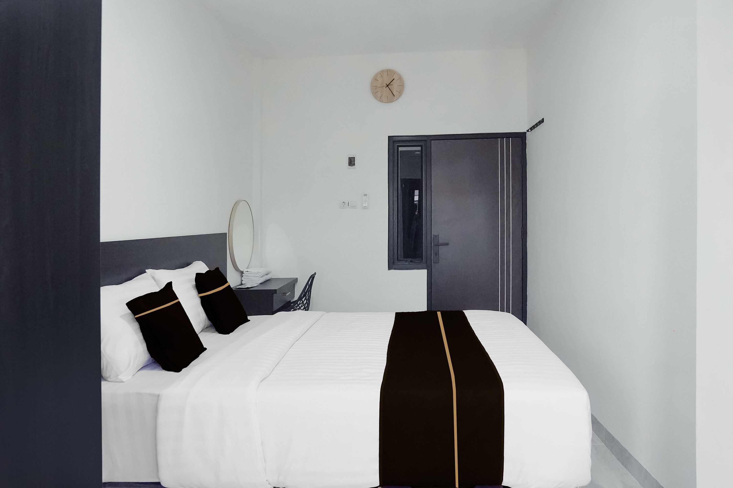 Habitación de hotel con cama, mesita de noche, espejo, reloj y armario.