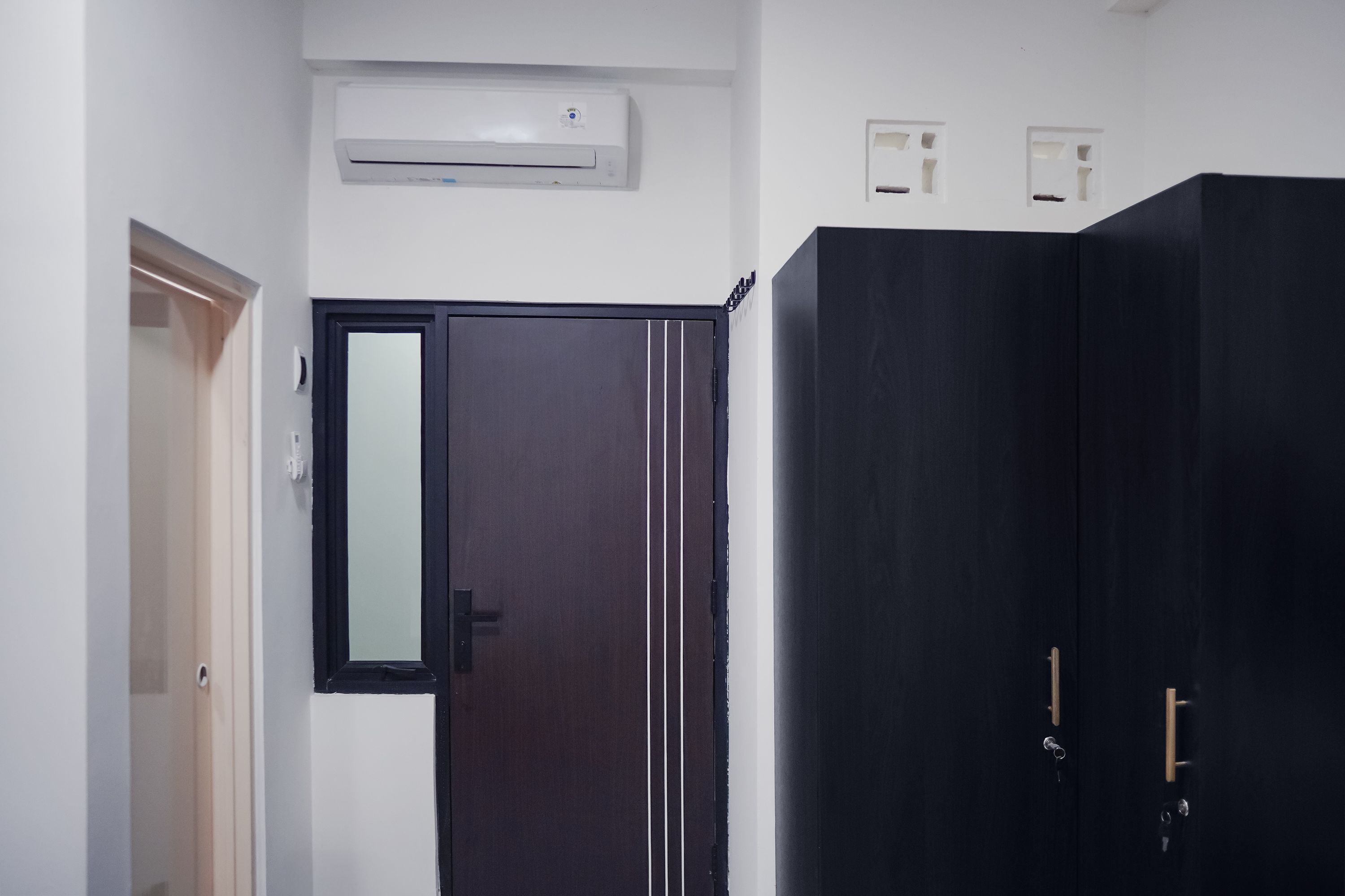 A room with a dark wooden wardrobe, a white wall-mounted air conditioner, and a door with a mirror.