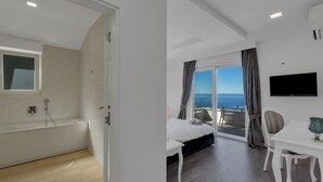 Een moderne hotelkamer met een badkuip, een bed, een eettafel, een televisie en uitzicht op zee.