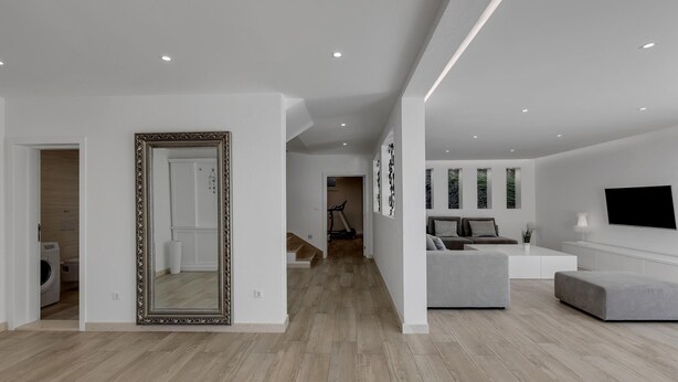 Een moderne woonkamer met een grote spiegel, een grijze bank, een salontafel en een flatscreen televisie aan de muur.