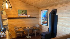 Een gezellig cabin interieur met houten wanden, een ronde tafel, twee stoelen, een open haard en kunstwerken aan de muur.