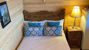 Une chambre dans un chalet en bois, avec un lit, une table de chevet, une lampe et un tableau au mur.