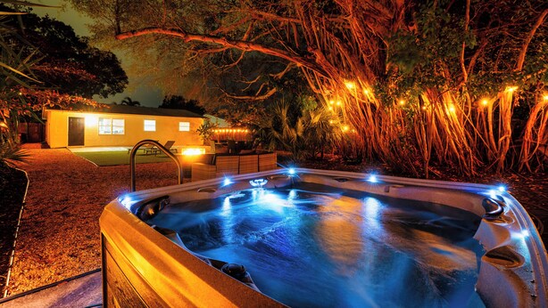 Un jacuzzi iluminado, rodeado de árboles y un edificio con luces.