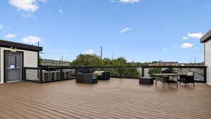 Une terrasse en bois avec des sièges extérieurs et une vue sur les bâtiments qui se dressent au loin.