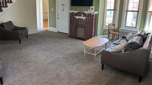 Ein Wohnzimmer mit Kamin, Fernseher, Sofa, Sessel und einer Treppe.