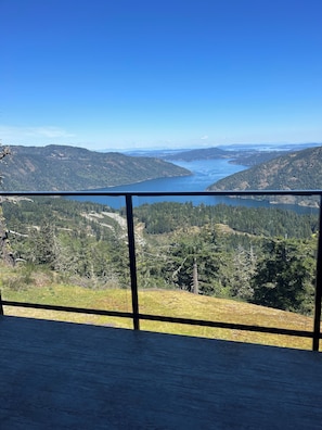 Une vue panoramique depuis un balcon donnant sur un lac, lui-même entouré de collines boisées.