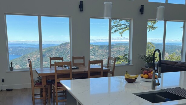Una cocina moderna con una isla grande, un comedor con sillas de madera y ventanas amplias que ofrecen una vista panorámica.