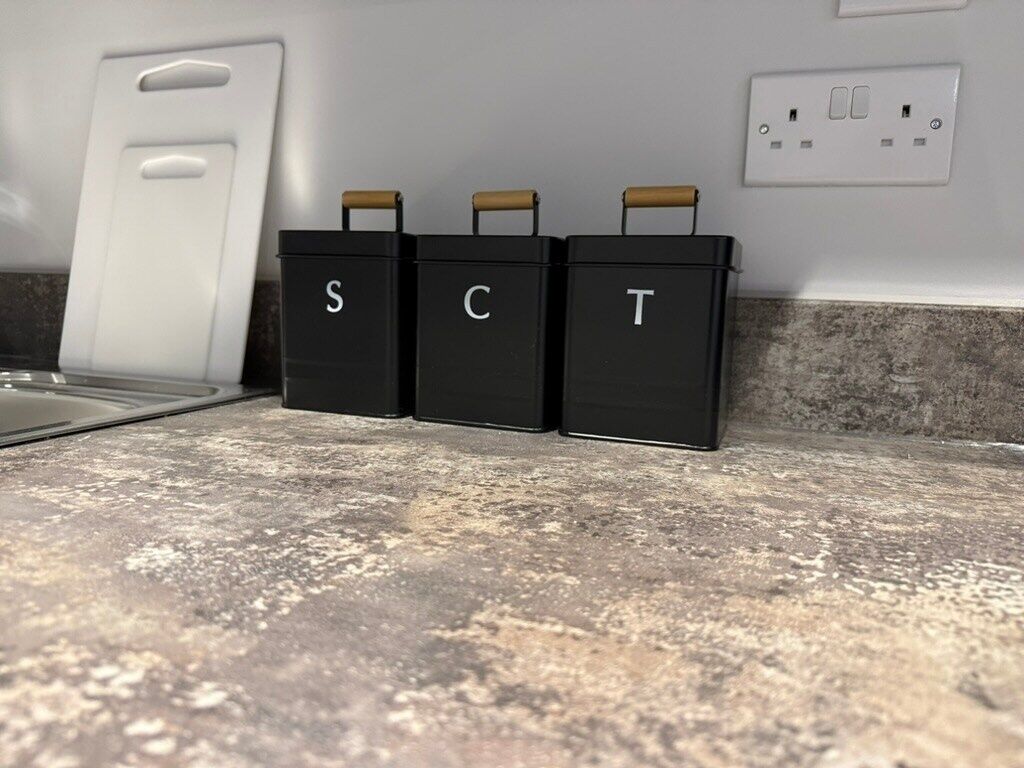 Three black storage bins labeled 'S', 'C', and 'T' on a kitchen countertop.