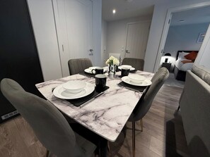 A modern dining area with a marble table, black and white plates, and a vase of flowers. - Stylish 2BR Flat •Parking• 6 min to Luton Airport (Luton)