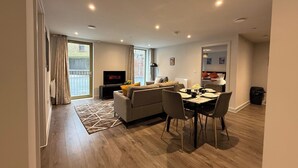 A modern living room with a sofa, dining table, and TV. - Stylish 2BR Flat •Parking• 6 min to Luton Airport (Luton)