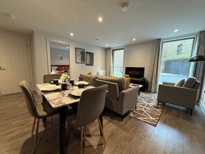 A modern living room with a dining area, a sofa, a TV, and a view of the outside. - Stylish 2BR Flat •Parking• 6 min to Luton Airport (Luton)