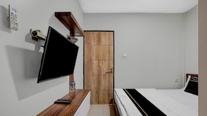 A bedroom with a TV mounted on the wall, a wooden desk with a remote control, a bed with a black and white striped bedspread, and a wooden wardrobe. - Collection O Yayah Residence  (Dramaga)