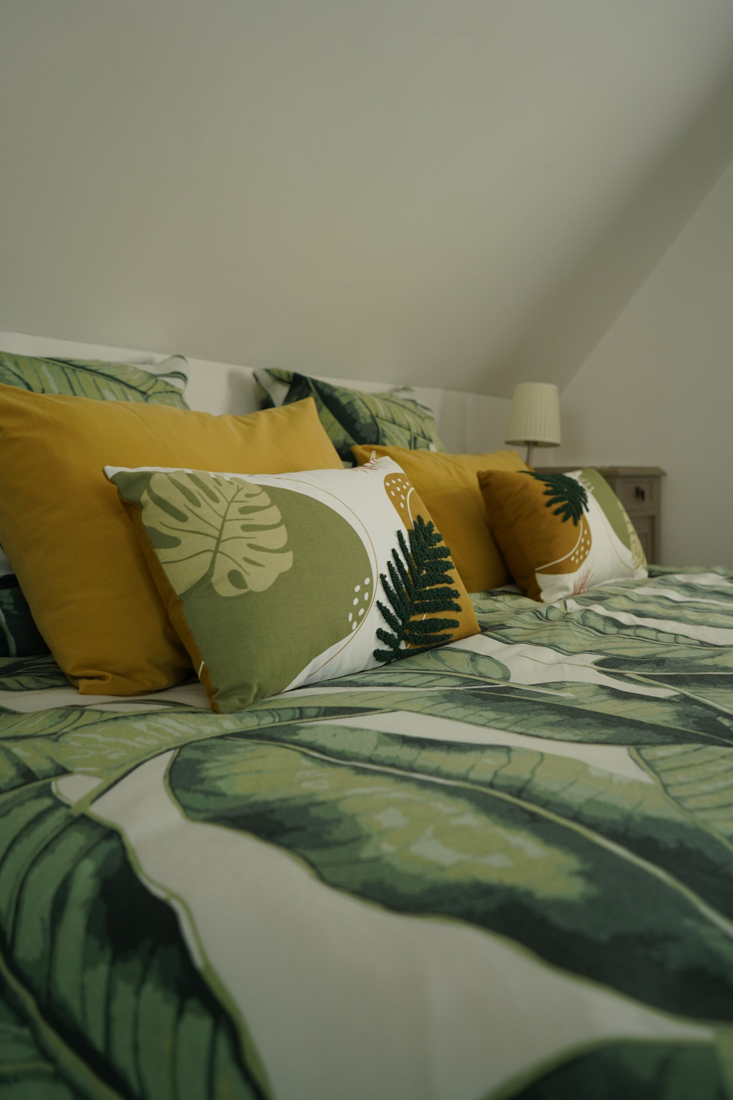 Een bed met een sprei met bladmotieven en drie kussens met bladerontwerpen.