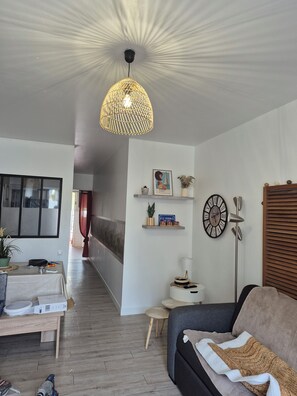 A modern living room with a sofa, a coffee table, a hanging light fixture, a wall clock, and a small side table. - townhouse (Le Verdon-sur-Mer)