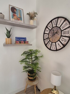 A wall clock with Roman numerals and a vintage design, a framed picture with a lighthouse, and a small potted plant on a shelf. - townhouse (Le Verdon-sur-Mer)