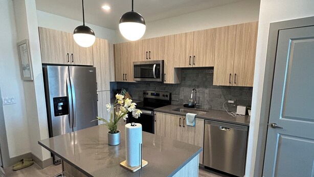 Una cocina moderna con una isla central, electrodomésticos de acero inoxidable y taburetes de bar.