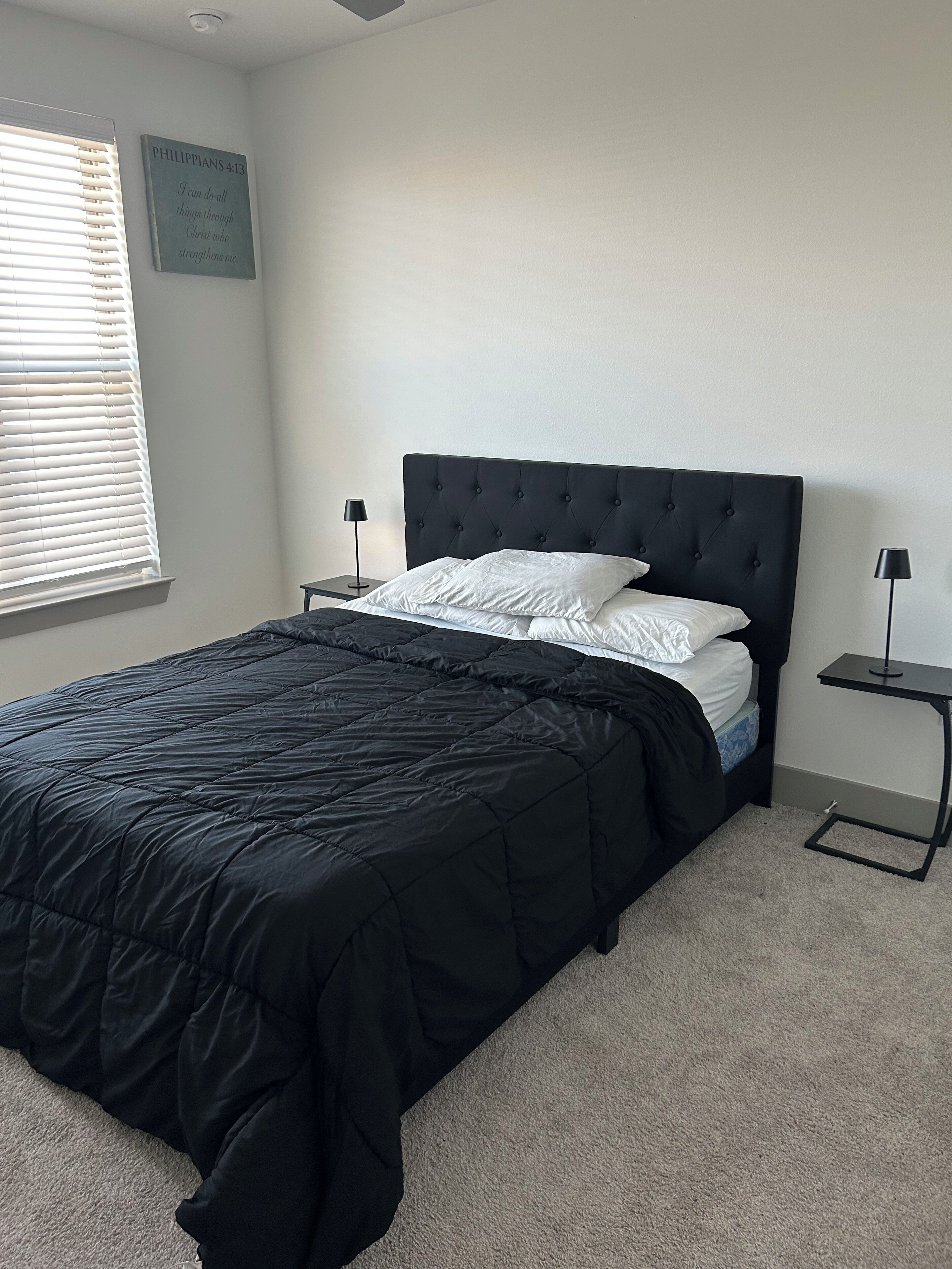 A bedroom with a black upholstered bed, white pillows, a black headboard, and two bedside tables with lamps.