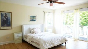 Ein Schlafzimmer mit Bett, Nachttisch, Deckenventilator und einem Fenster mit Vorhängen.