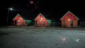 Three wooden cabins with snow on the ground, each decorated with holiday lights. - "Seacoast" Cabin at Keyser Pond Campground (Henniker)