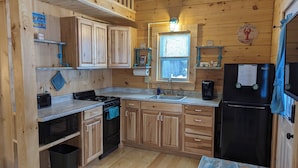 A compact kitchen with wooden cabinets, a stove, a sink, and a refrigerator. - "Seacoast" Cabin at Keyser Pond Campground (Henniker)