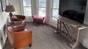 Een woonkamer met een grote flatscreen televisie, een bruine leren fauteuil, een roze fauteuil en een houten salontafel.