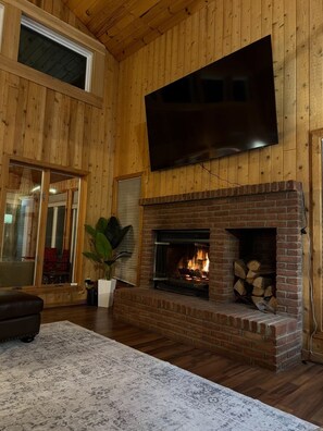 A living room with a brick fireplace, a flat-screen TV mounted above it, and a large window.
