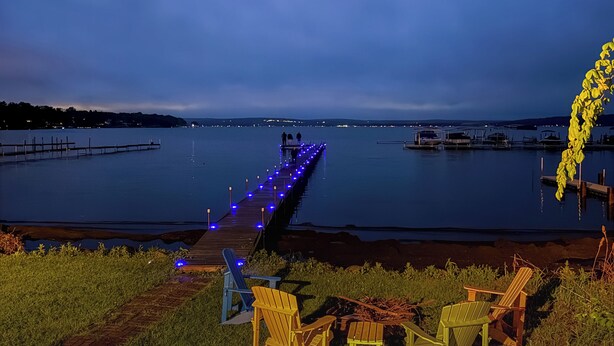 Vista de un lago con un muelle, sillas y un bote.