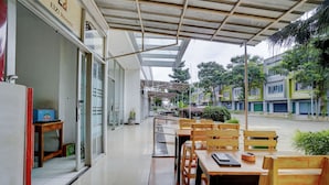 Un espacio de estar al aire libre techado, con mesas y sillas de madera, un cartel de 'Elizi Rooms' y vistas a una calle con edificios.