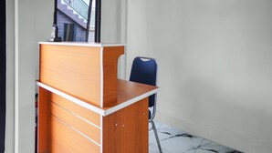 A wooden desk with a chair in a room with white walls and a tiled floor. - Hotel O Roda Inn (Padang)