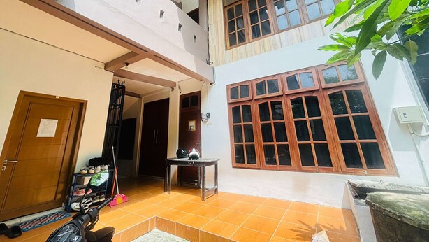 A multi-level residential building with a tiled patio, a wooden door, a shoe rack, and a table with a helmet. - OYO 95097 Griya Asri Guest House (Depok)