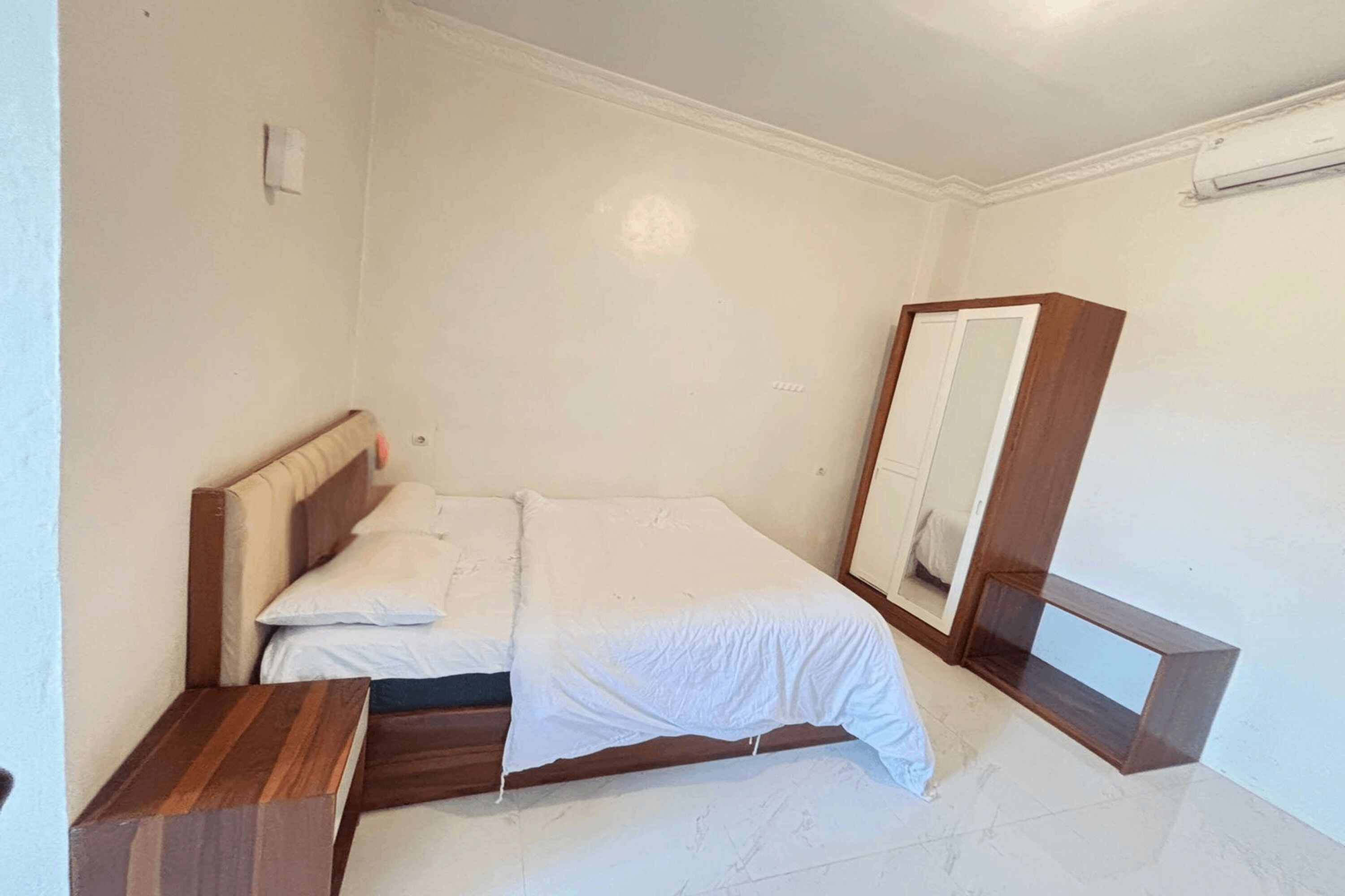 A bedroom with a wooden bed, a nightstand, a mirror, and a white wall.