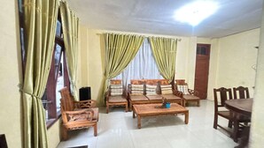 A living room with wooden furniture, including sofas and a coffee table, and a dining table with chairs. - OYO 95097 Griya Asri Guest House (Depok)
