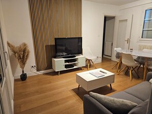 A modern living room with a flat-screen TV, a dining table with chairs, a white sofa, and a decorative plant.