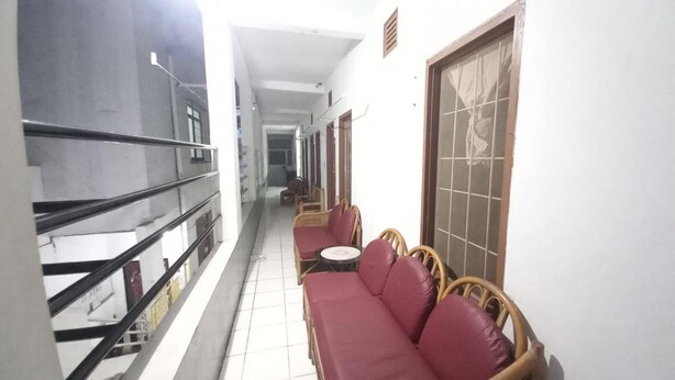 A narrow corridor with a balcony on one side, a seating area with wicker furniture and red cushions, and a tiled floor. - OYO 95096 Dewi Sudirman Guest House (Bandung)