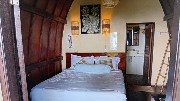 Una cama bien hecha en una habitación con paneles de madera y un baño pequeño a la vista a través de una puerta abierta.