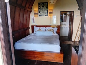 A neatly made bed in a room with wooden paneling and a small bathroom visible through an open door. - OYO 95104 Lisa Homestay  (Denpasar)