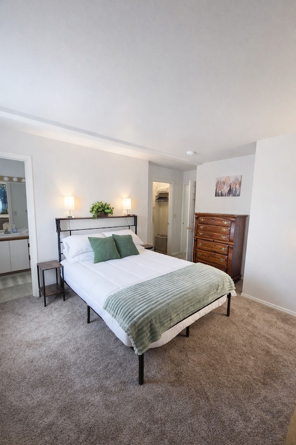 A bedroom with a bed, bedside tables, a dresser, a mirror, and a door leading to a bathroom.