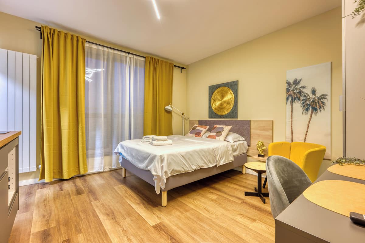 A hotel room with a bed, a desk, a chair, a lamp, and a painting on the wall.