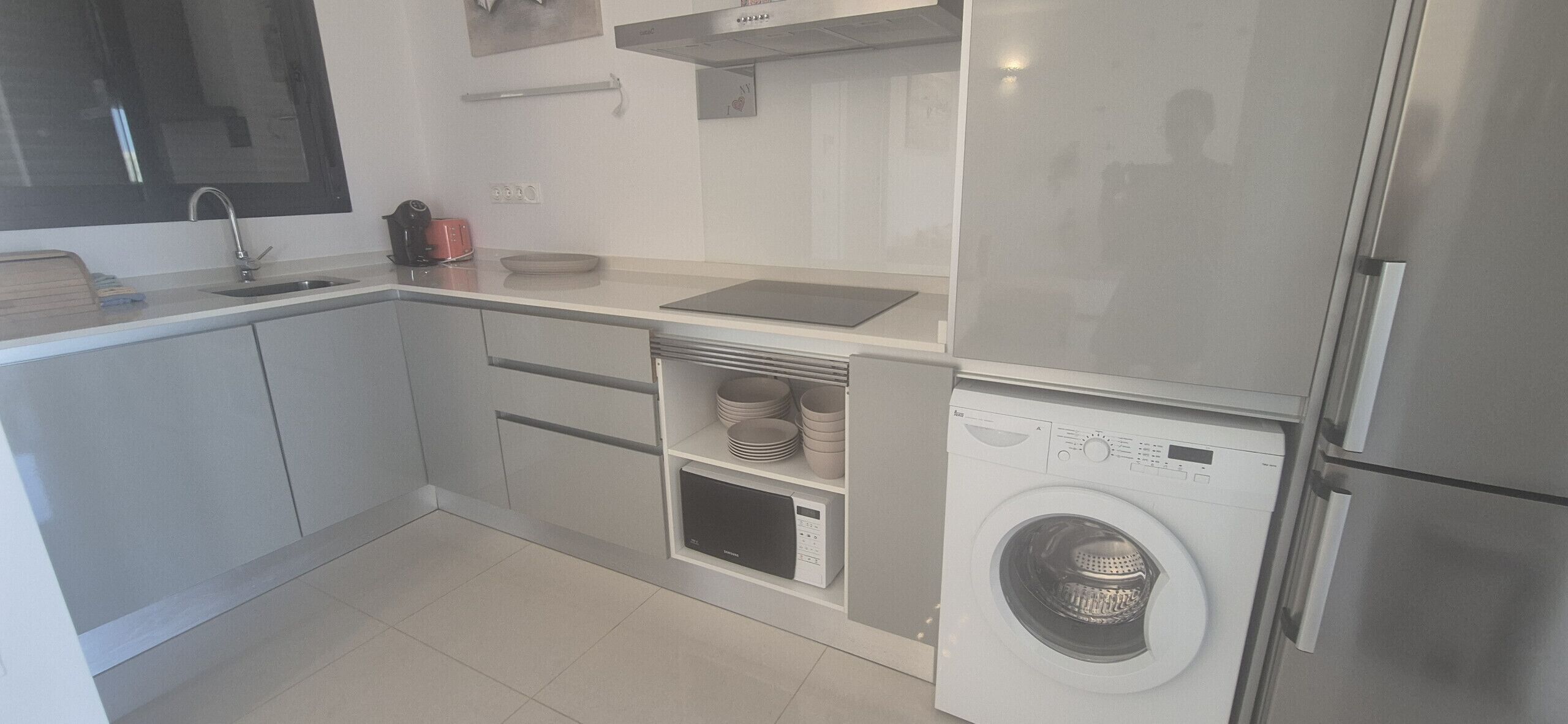 Eine moderne Küche mit Waschmaschine, Edelstahlkühlschrank und Mikrowelle.