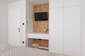 A bedroom with a bed, a white wardrobe, a wooden panel wall, a mounted TV, and a small stool. - Kresevo Family Villa With Heated Pool (Sestanovac)
