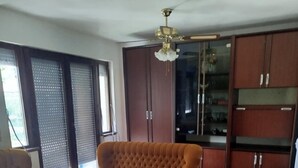 Un soggiorno con un divano marrone, un tavolino da caffè in legno e poggiapiedi coordinati. Si nota una ventola a soffitto, un'ampia finestra con persiane e mobili contenitori in legno.