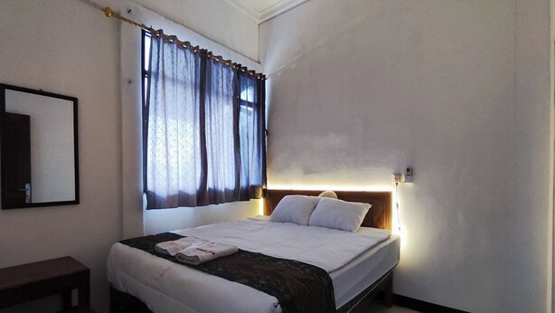 A neatly made bed with a headboard, a bedside table, and a window with curtains. - OYO 95106 A Homestay Syariah (Sambi)