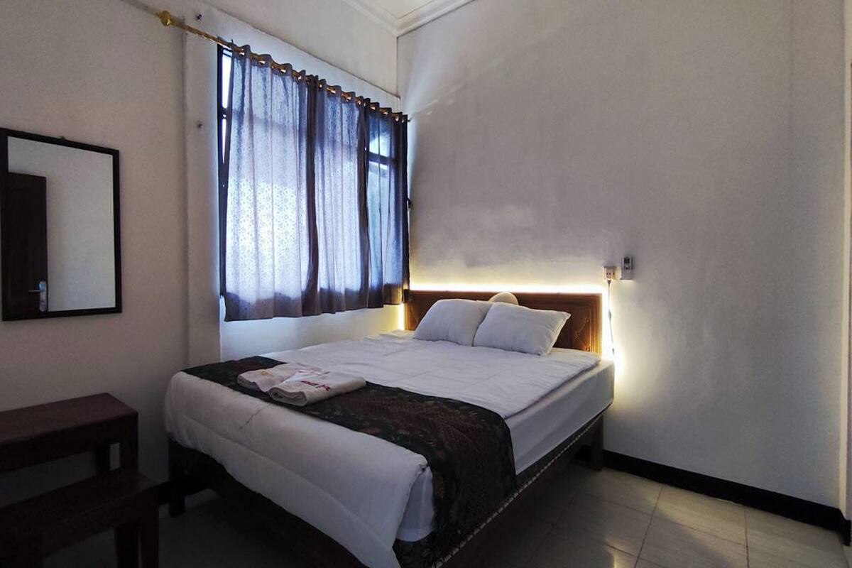 A neatly made bed with a headboard, a bedside table, and a window with curtains.